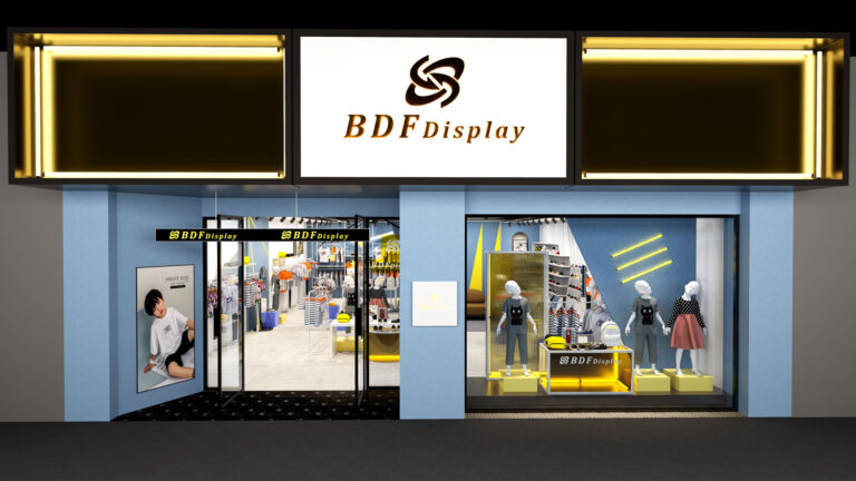 Modern kids retail store entrance featuring light blue facade, illuminated BDFDisplay signage, glass entry doors, and mannequin window display risers
